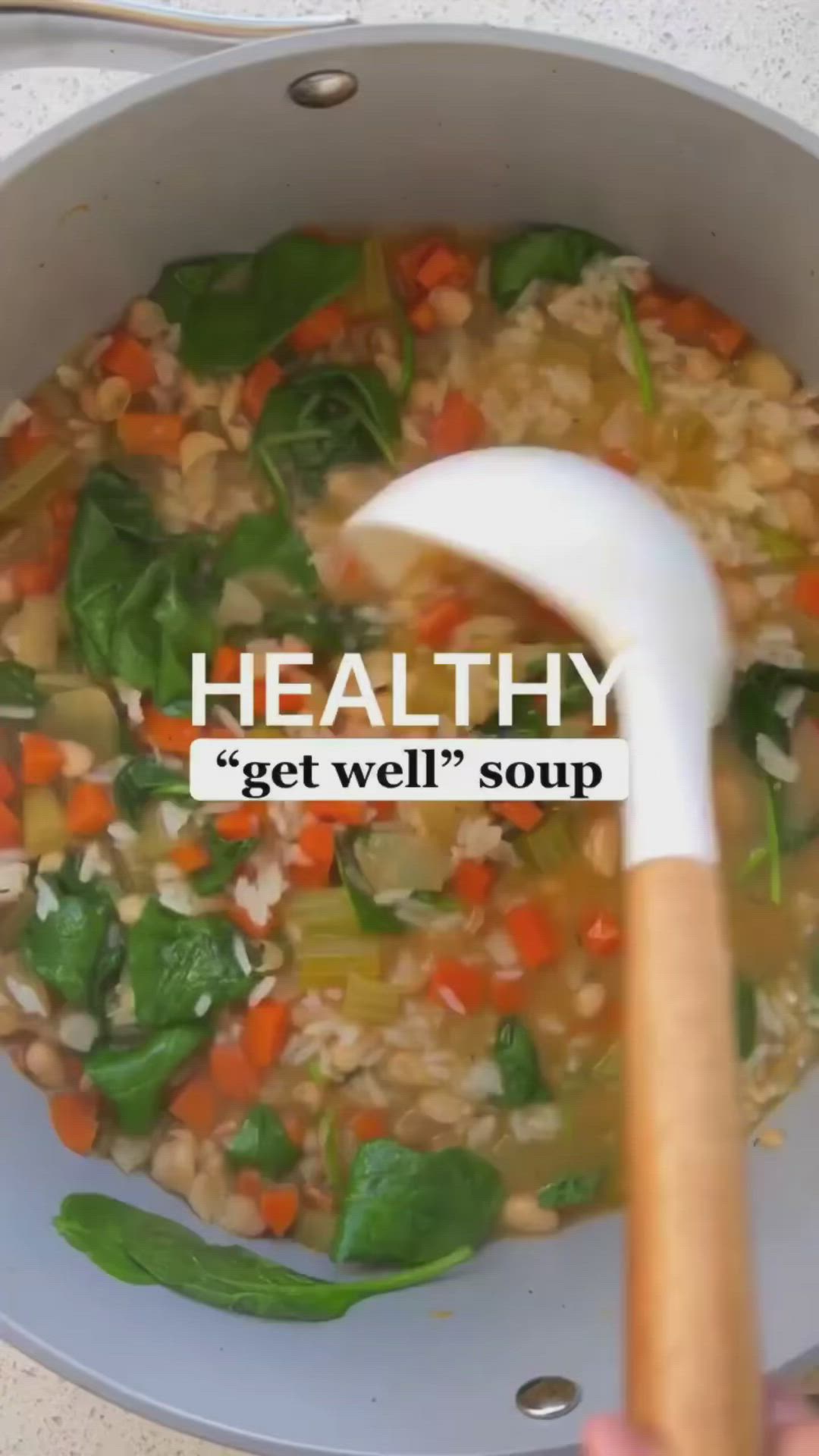 This may contain: a person holding a wooden spoon in a pot filled with vegetables and barley soup that reads healthy get well soup