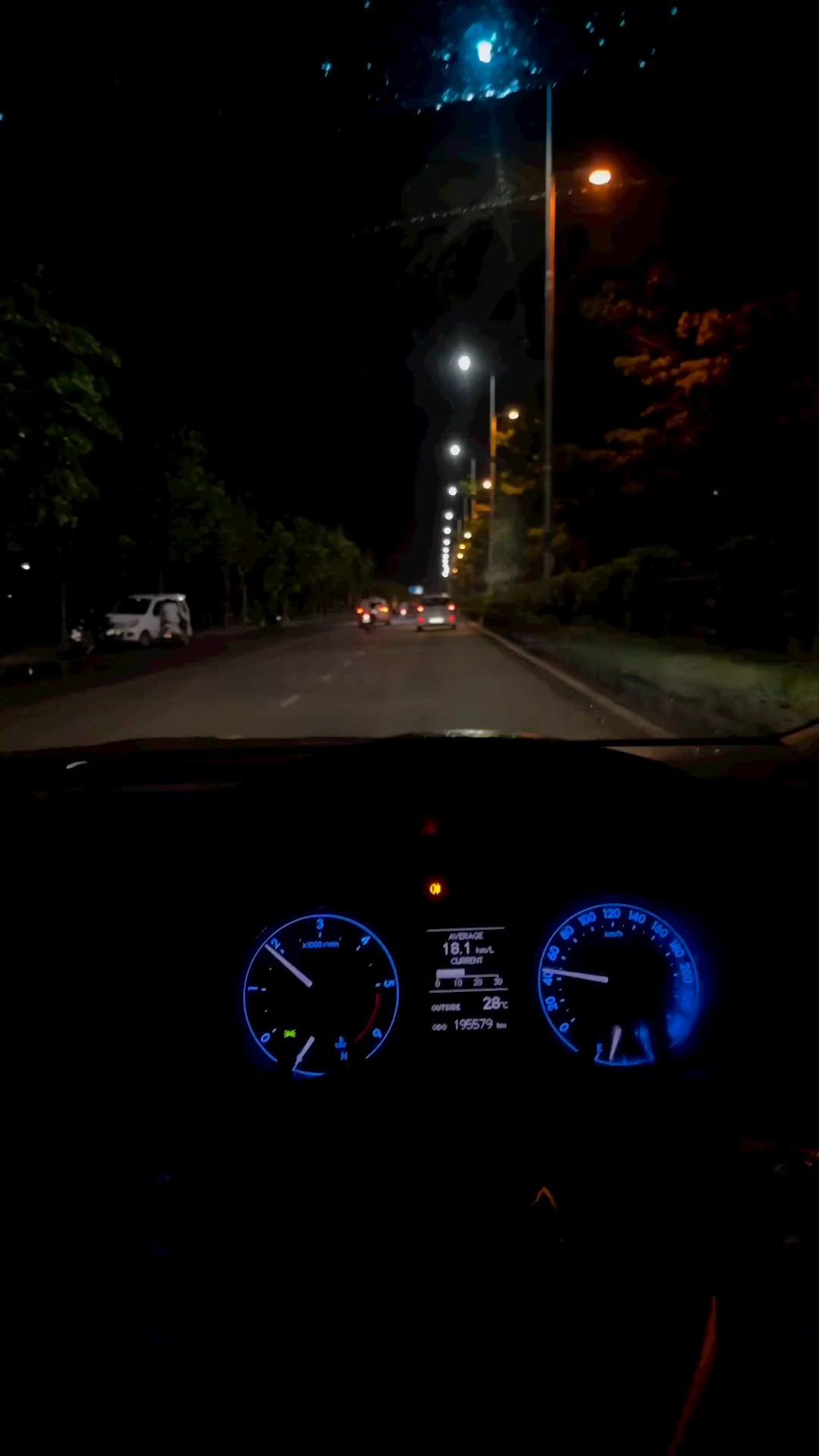 This may contain: the dashboard of a car is lit up at night with street lights and trees in the background