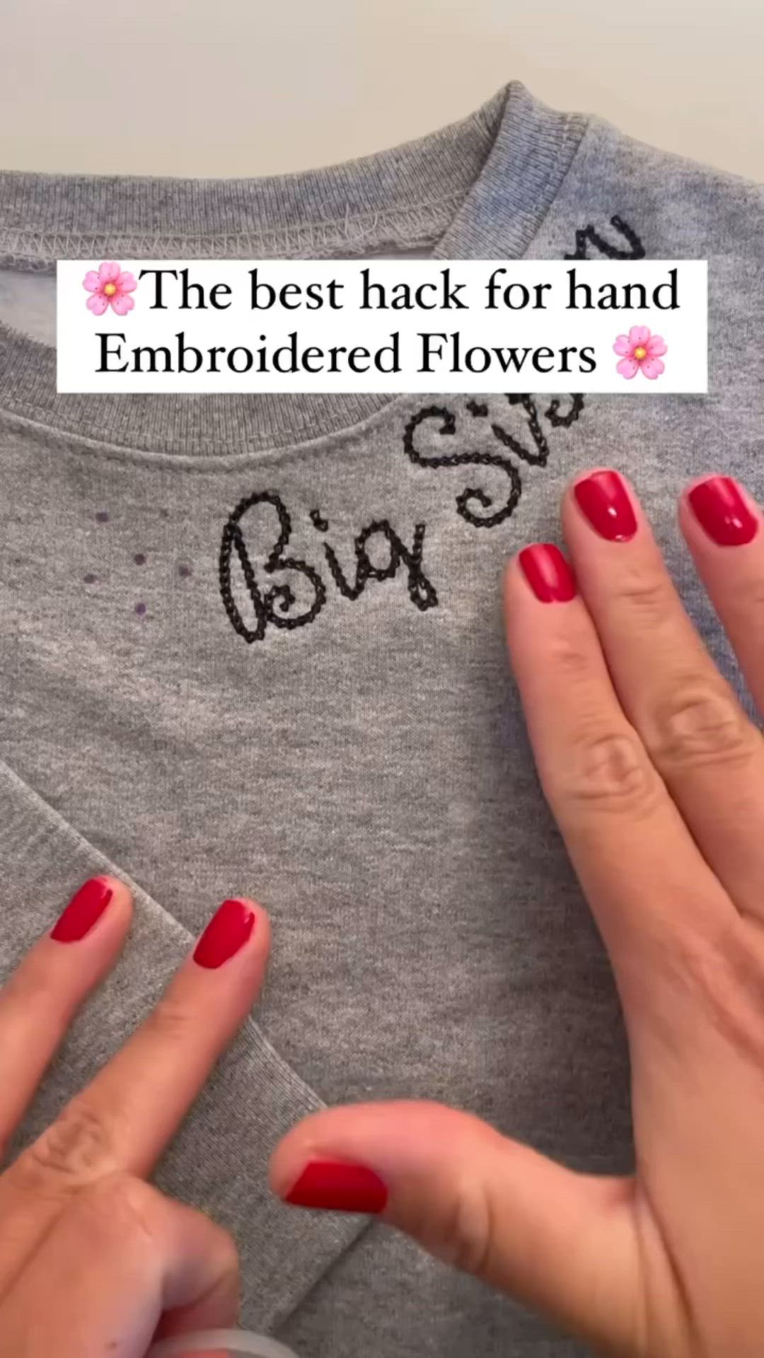 This may contain: two hands with red nail polish holding onto a grey t - shirt that says, the best hack for hand embroidered flowers