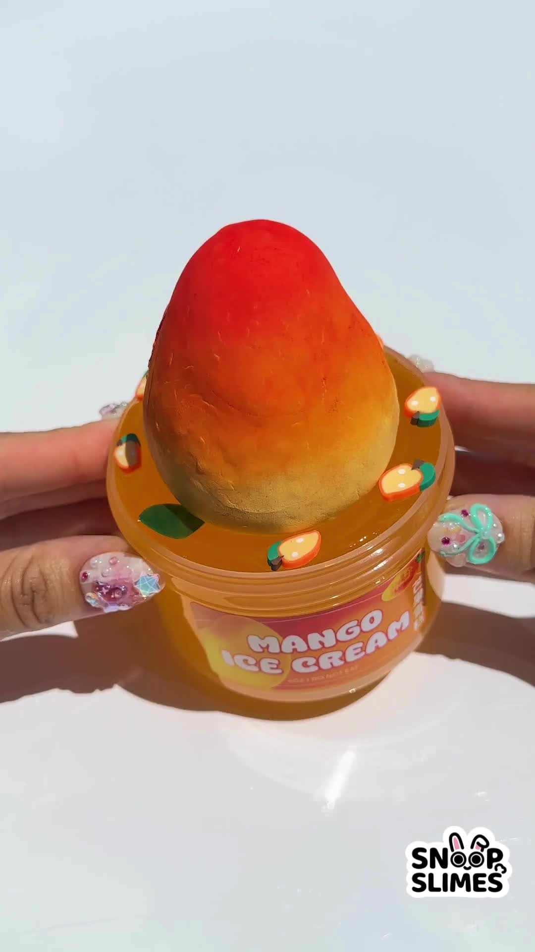 This may contain: an orange ice cream sits in a plastic container on someone's hand, with candy around it