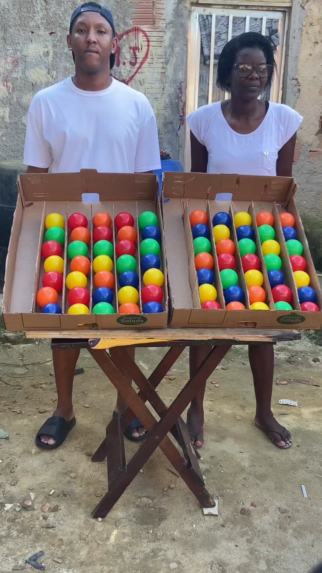 This may contain: two people standing next to each other with boxes of balls in front of them