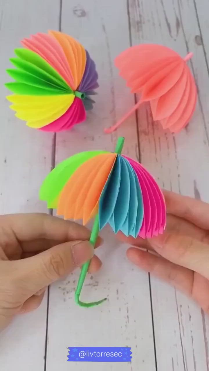 This may contain: someone is holding some colorful paper umbrellas in their hands on a white wooden table