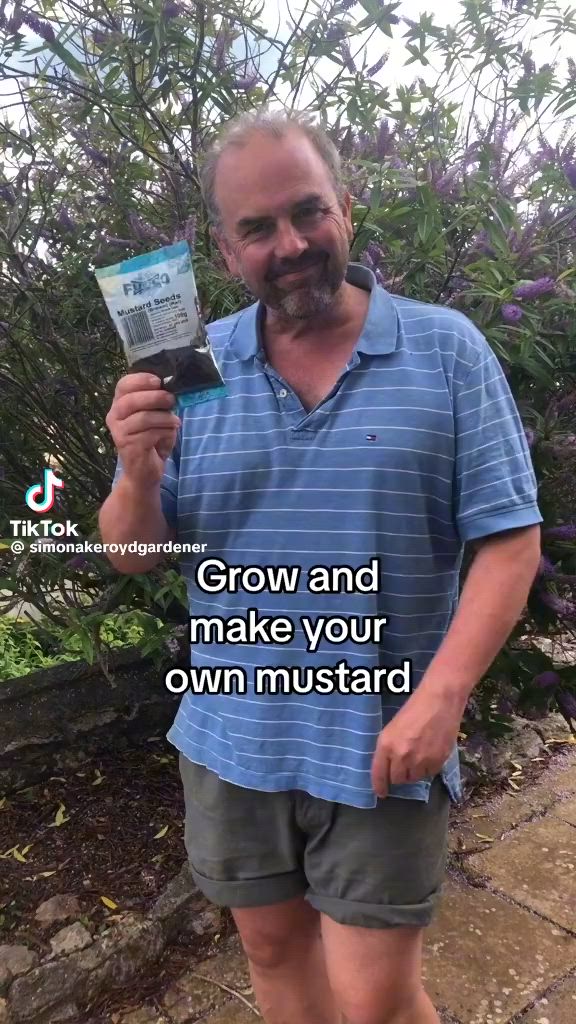 This may contain: a man standing in front of purple flowers holding up a card with the words grow and make your own mustardard