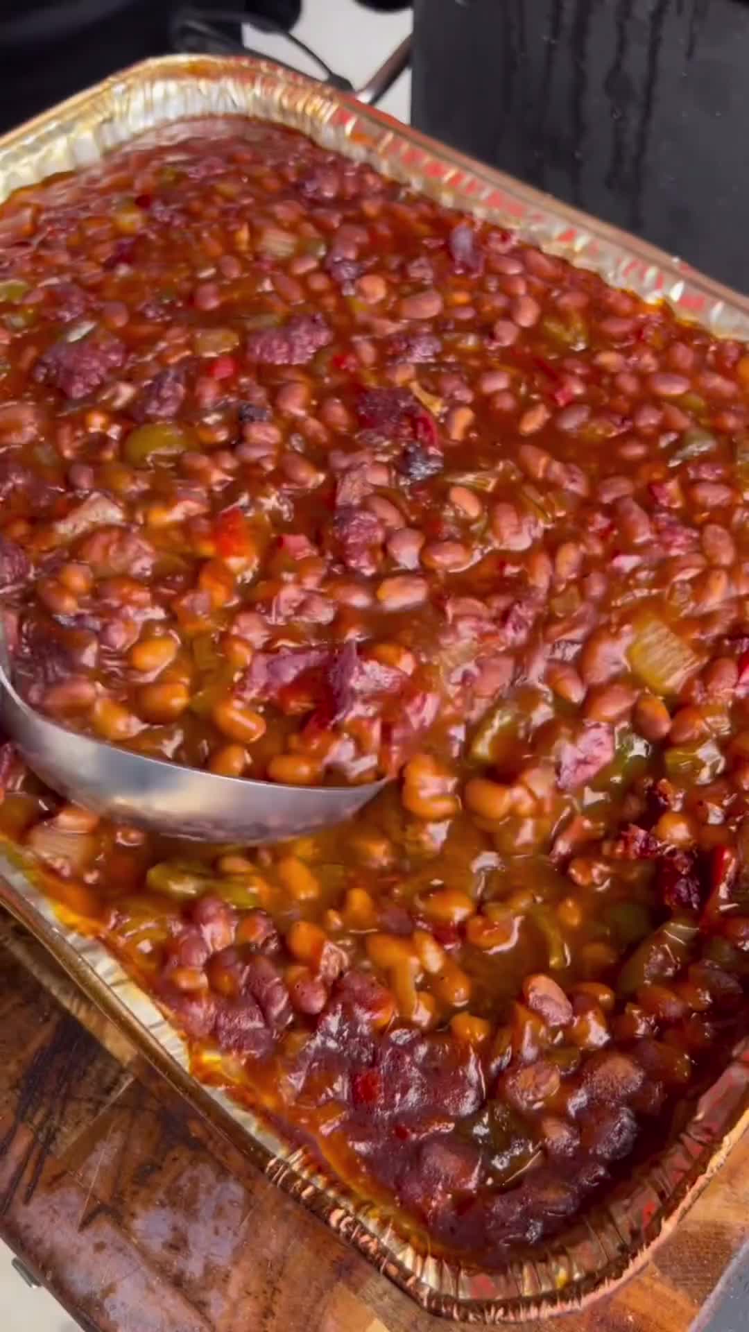 This may contain: a baked dish with beans in it on a wooden cutting board