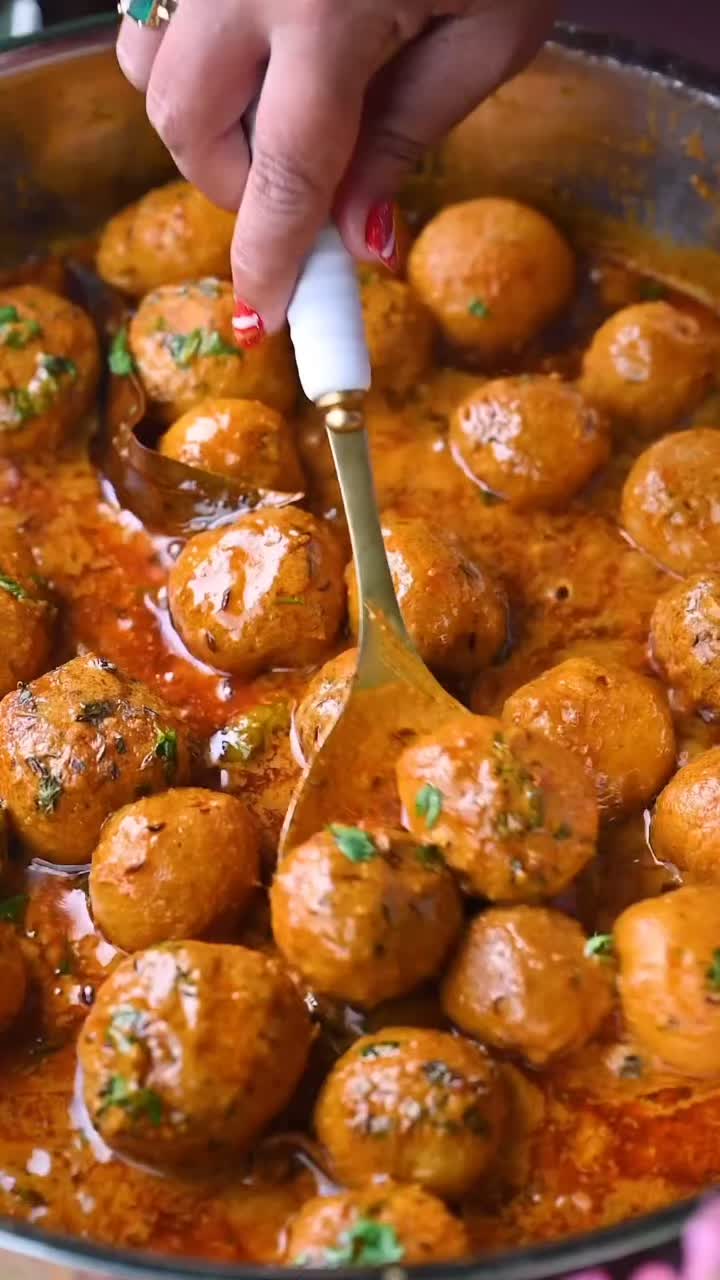 This may contain: a person is spooning some meatballs out of a pan with sauce on it