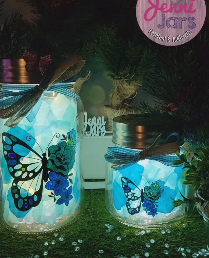 This may contain: two jars with butterflies painted on them sitting in the grass next to flowers and plants