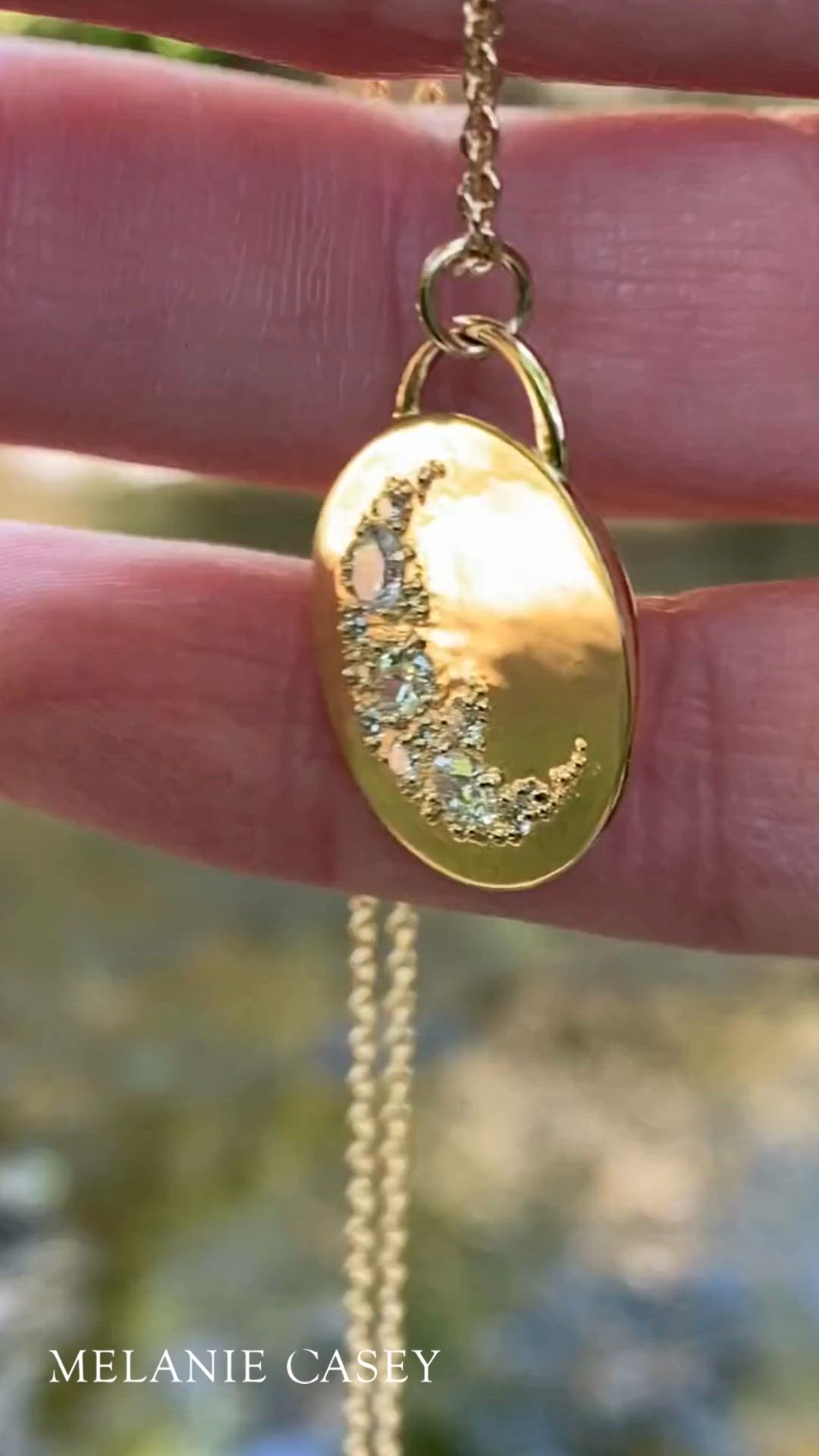 This contains: A woman's hand holding a large gold and diamond pendant hanging from a chain.