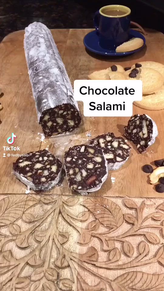 This may contain: chocolate salami on a cutting board next to some cookies and a cup of coffee