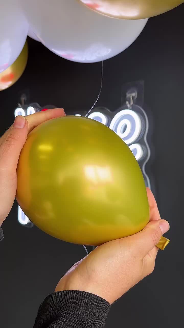 This may contain: a woman is cutting balloons with scissors in front of a wall decorated with gold and white balloons