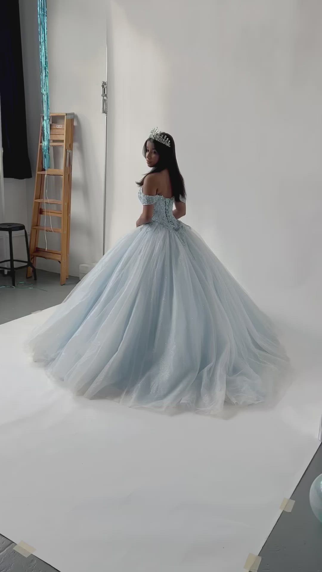 This may contain: a woman in a blue dress is standing on a white backdrop and posing for the camera