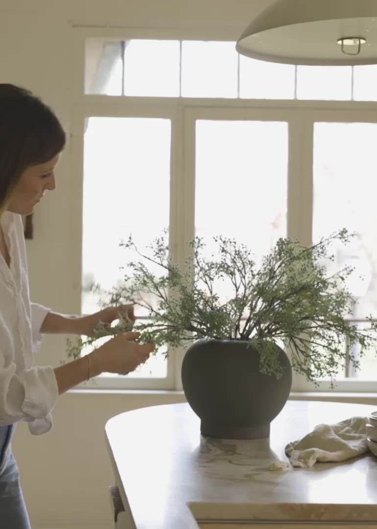 This may contain: a woman standing in front of a table with a vase filled with flowers on it