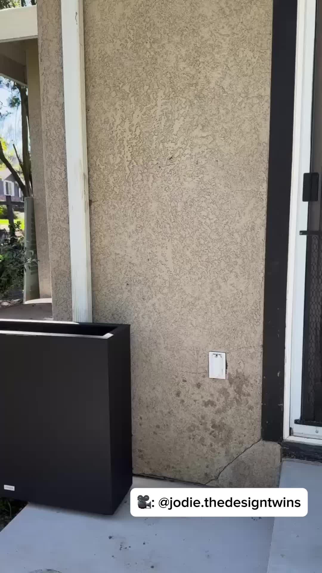 This may contain: a man is holding up a black box in front of a building that says amazon cedar tree privacy screen