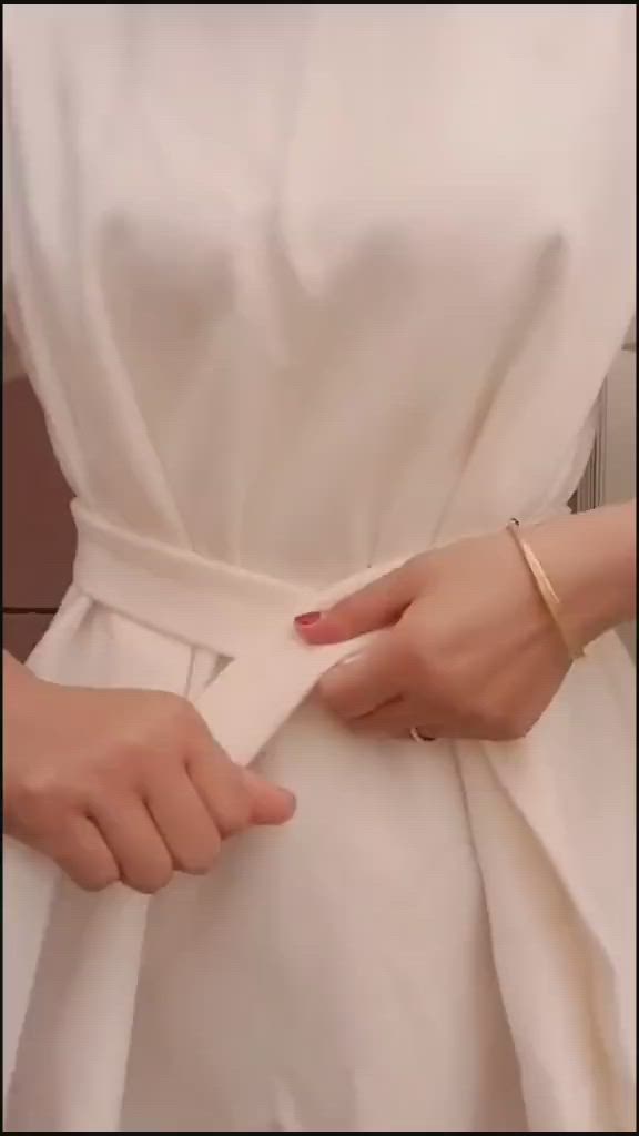 This may contain: a woman wearing a white dress with a gold ring on her left hand and an arm wrapped around the waist