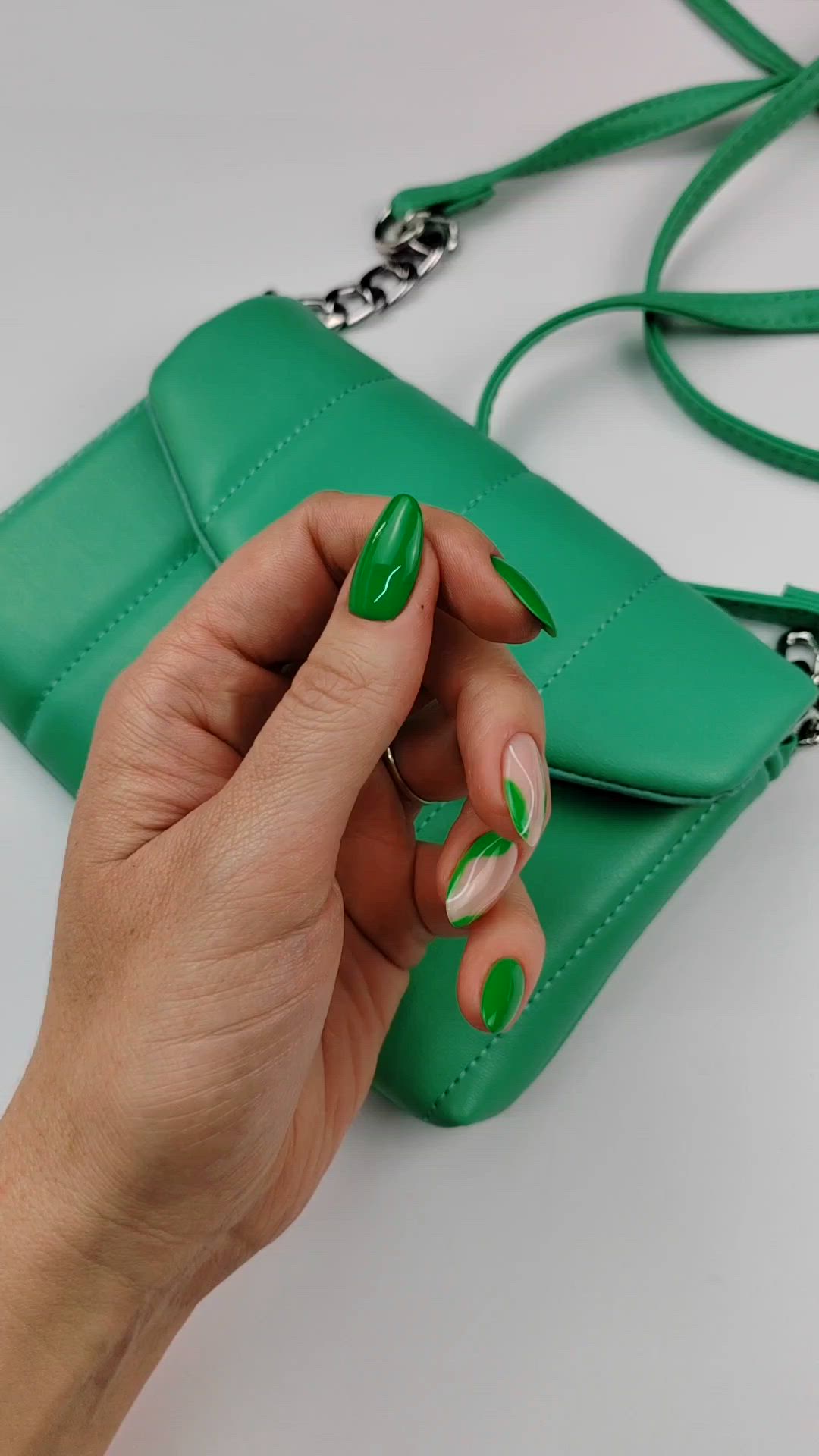 This may contain: a woman's hand with green and white nail polish holding onto a green purse