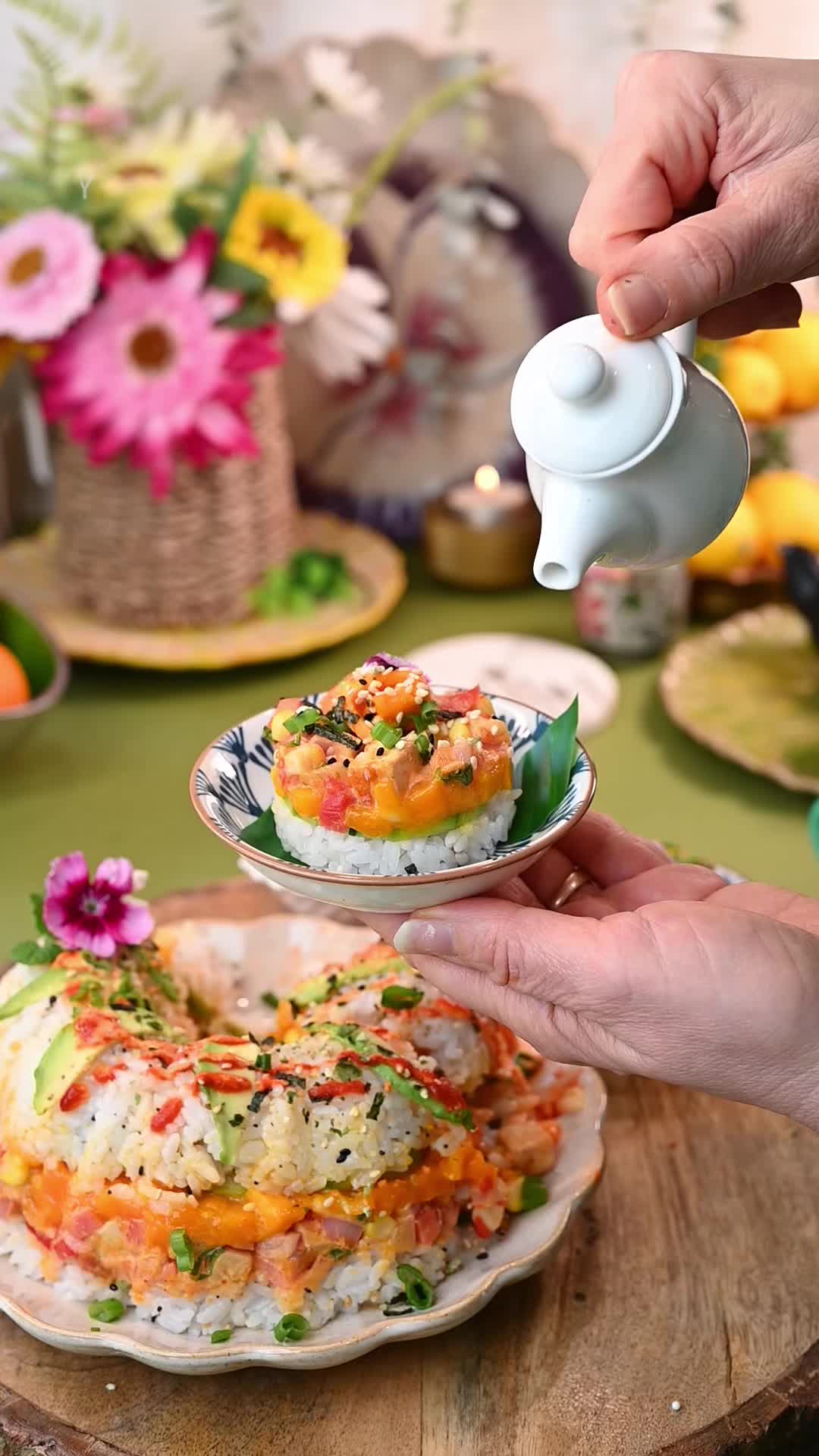 This may contain: a person holding a plate with sushi cake on it and flowers in the background