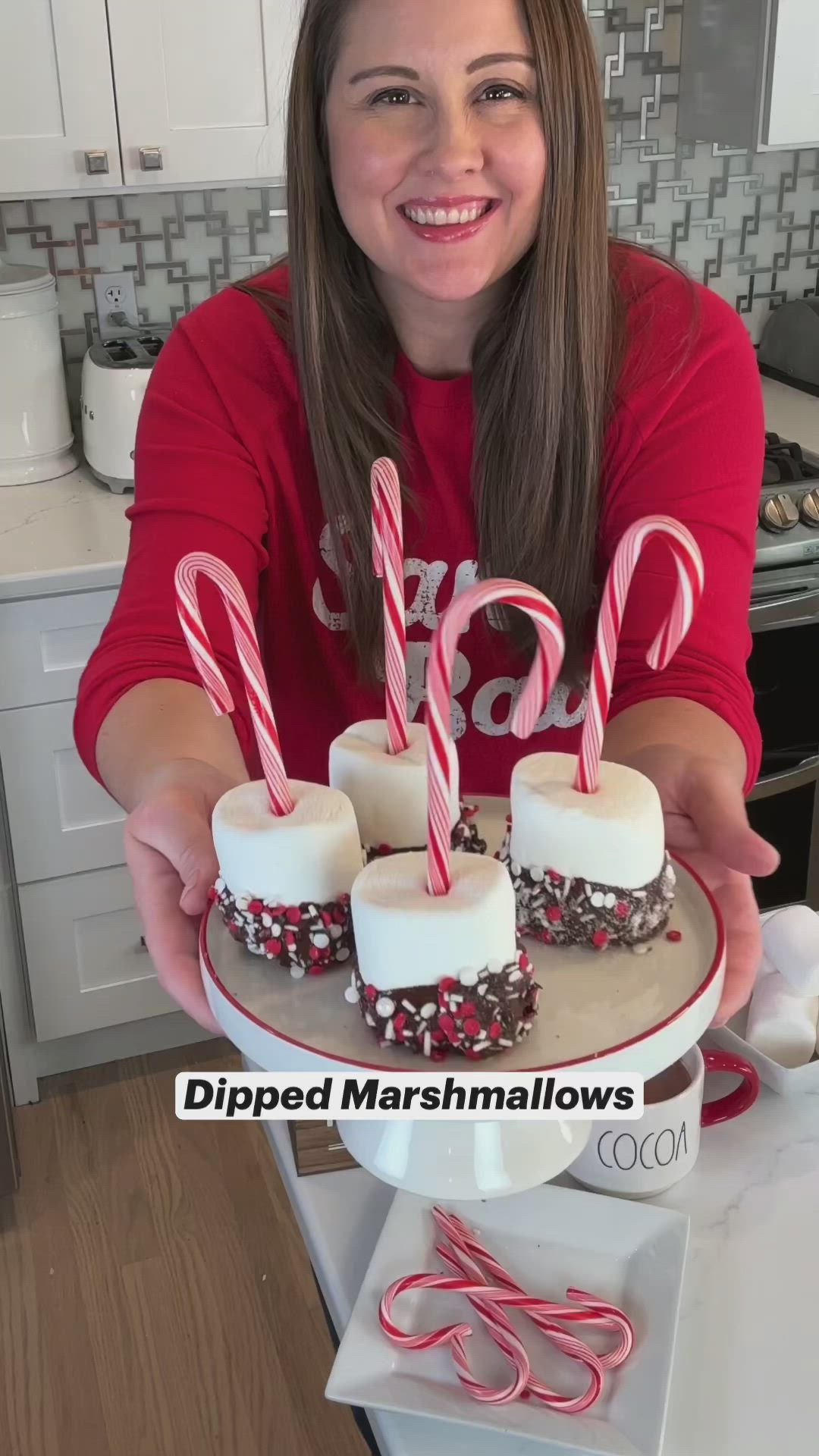 This may contain: a woman holding a cake with marshmallows and candy canes on it