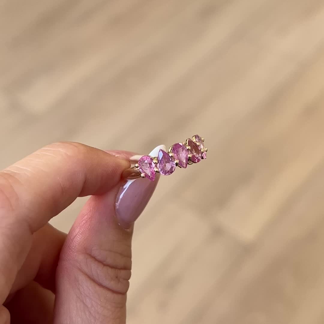 This may contain: a person holding a ring with pink stones on it