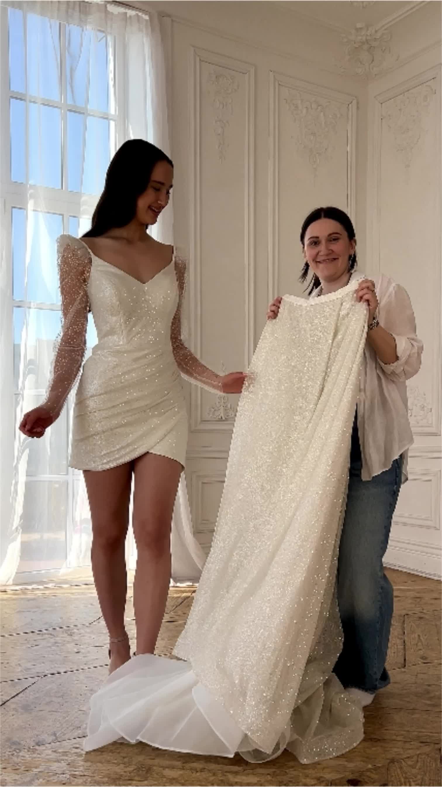 This may contain: two women standing next to each other in front of a white wall holding up a dress