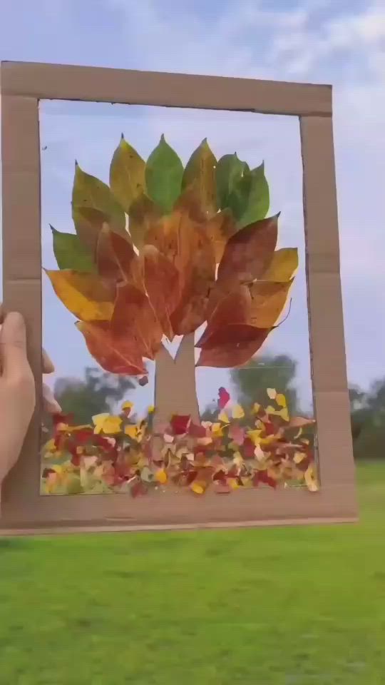 This may contain: a person holding up a cardboard box with leaves on it in front of a grassy field