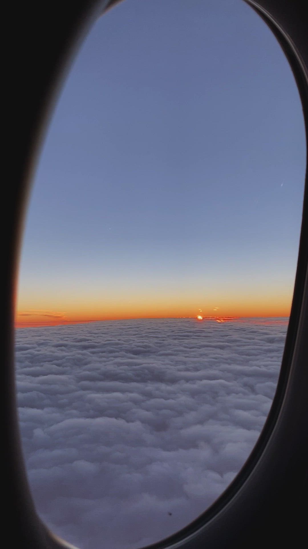 This may contain: an airplane window with the sun setting in the sky as seen through it's clouds