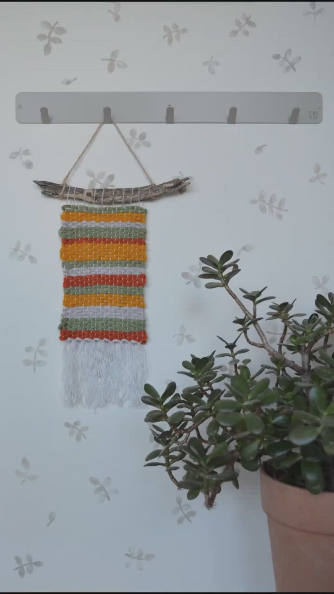 This may contain: a wall hanging made from yarn with a potted plant next to it