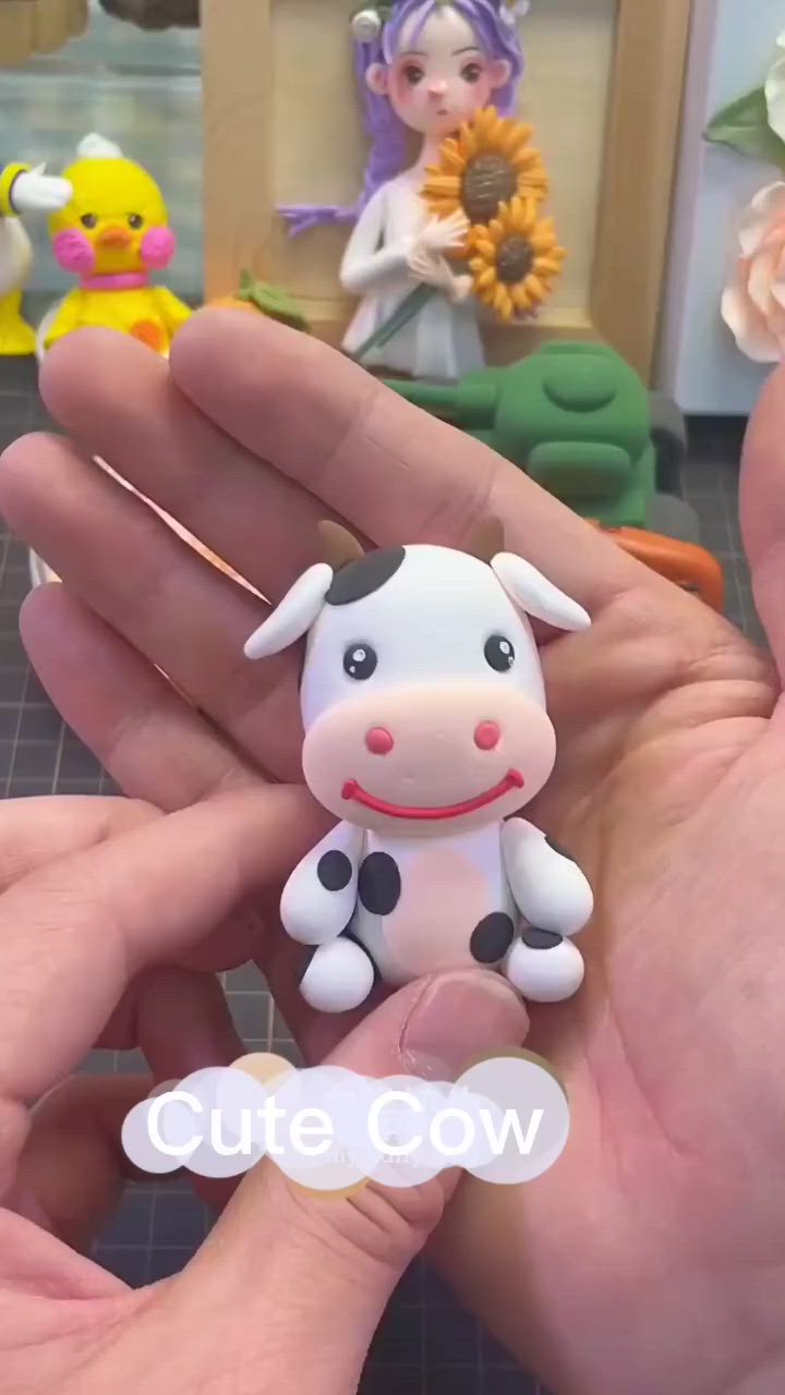 This may contain: a hand holding a small toy cow in it's right hand, with other figurines on the background