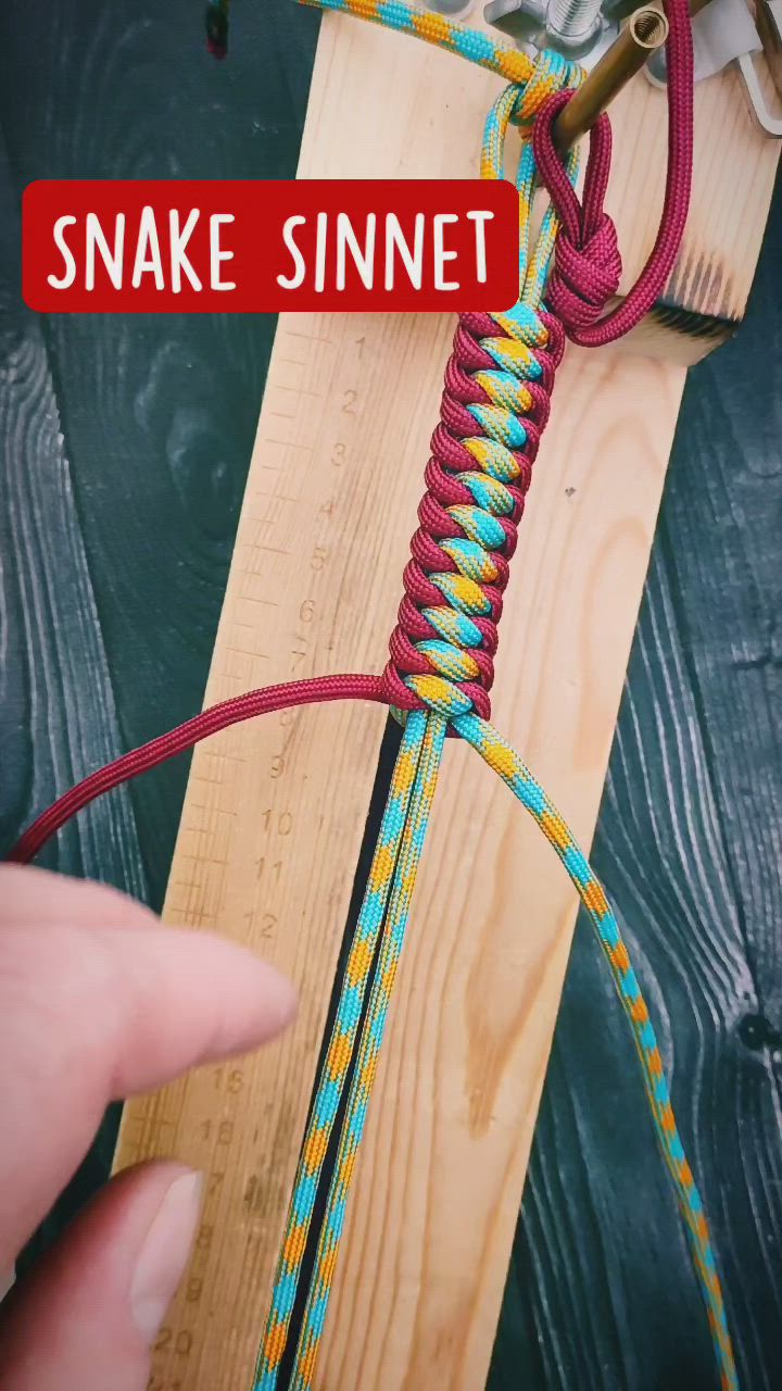 This may contain: someone is making a snake sinnet on a piece of wood with red and blue thread