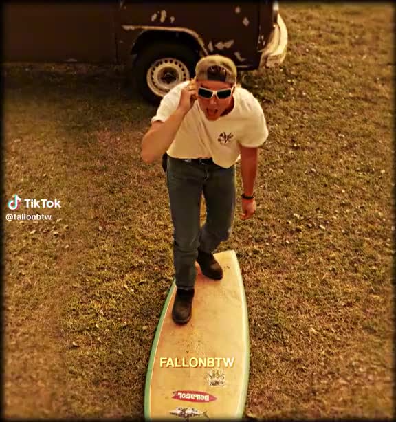 This may contain: a man standing on top of a surfboard in the grass with his mouth open