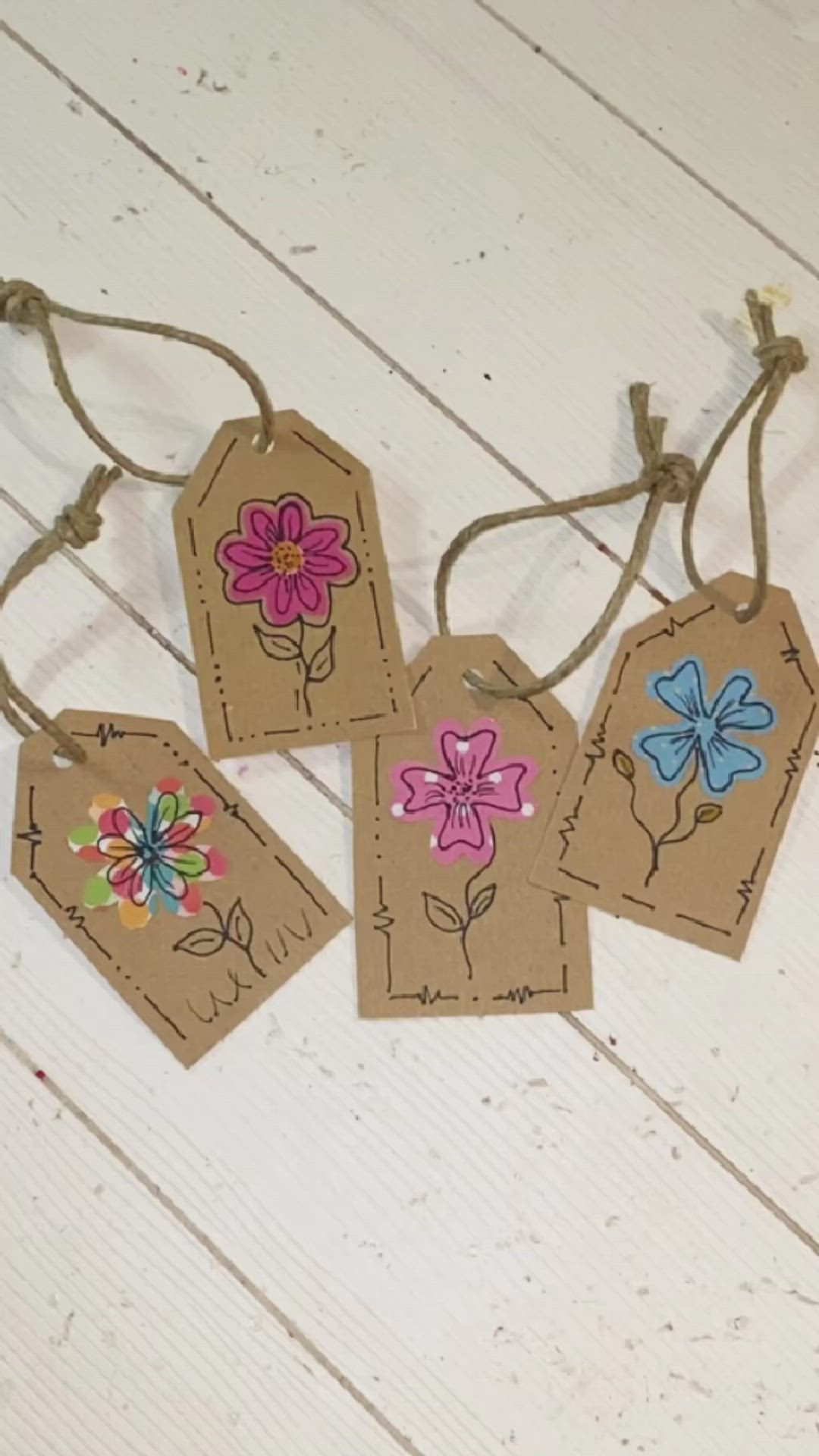 This may contain: four tags with flowers on them are hanging from twine strings against a white wooden background