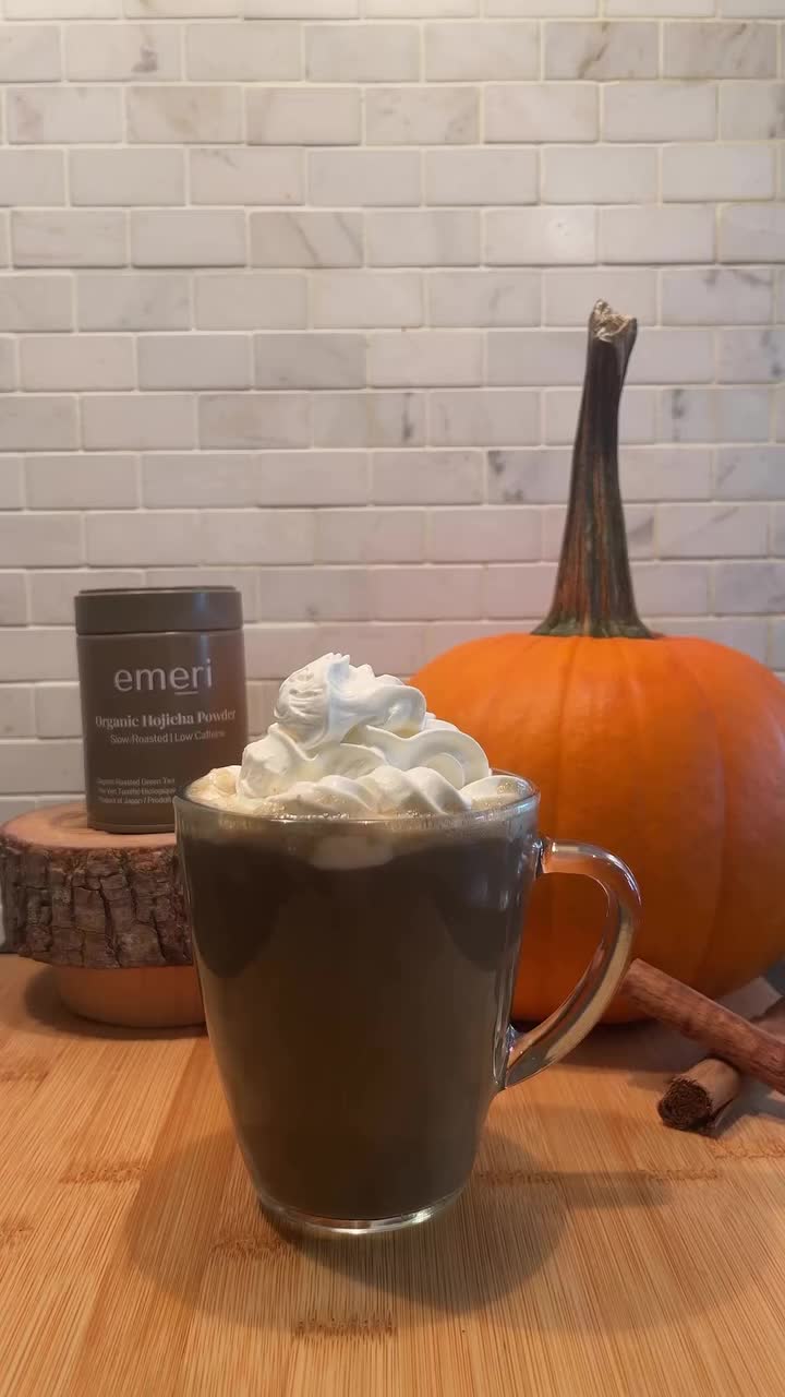 This may contain: a cup of hot chocolate with whipped cream in it on a table next to pumpkins