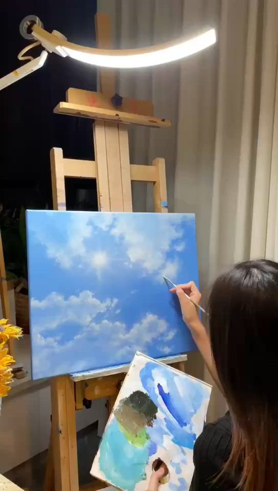 This may contain: a woman is painting clouds on an easel