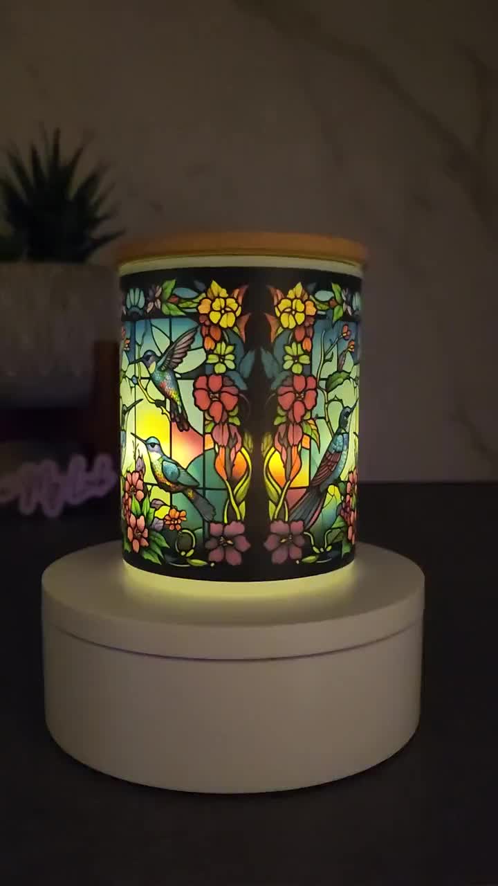 This may contain: a stained glass candle holder sitting on top of a white stand next to a potted plant