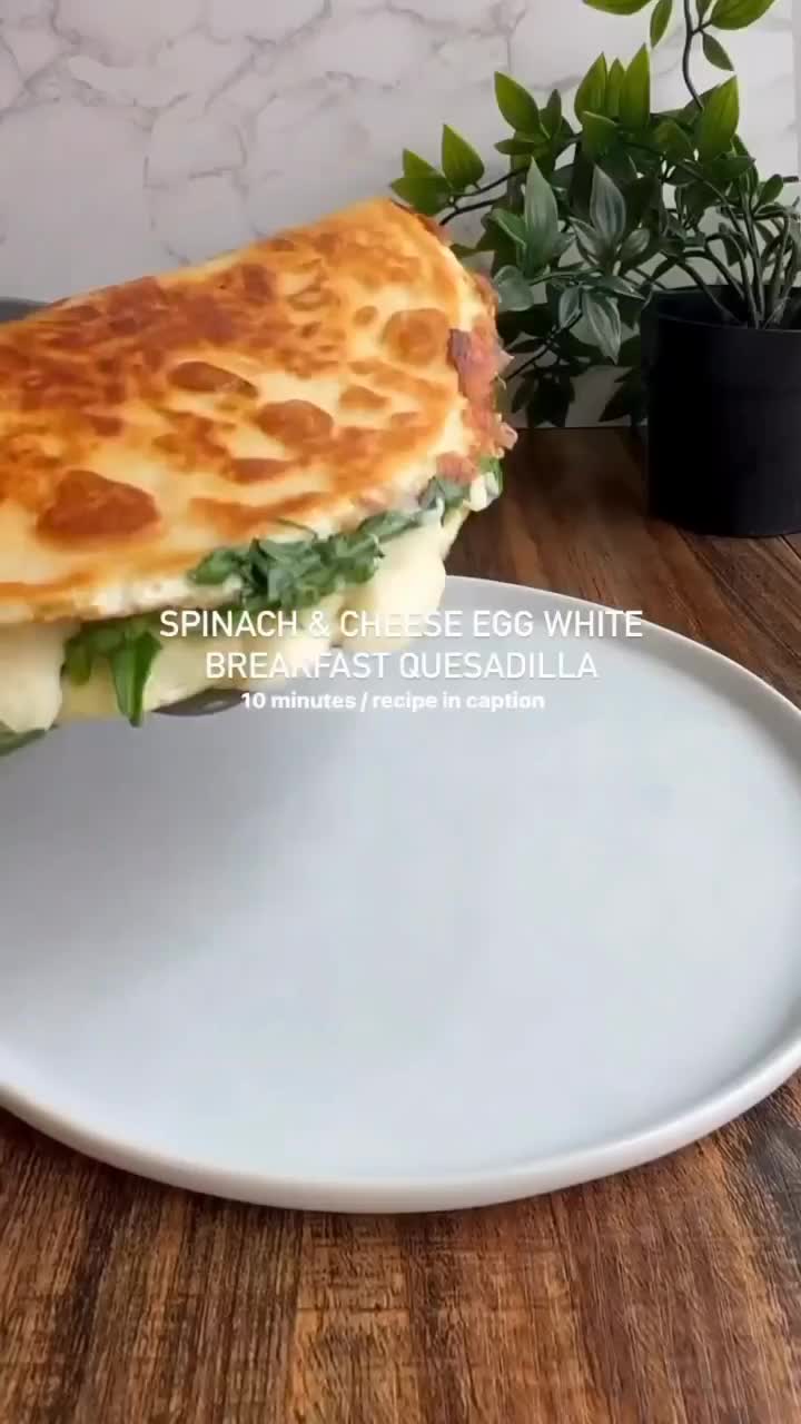 This may contain: a sandwich on a white plate sitting on a table next to a potted plant