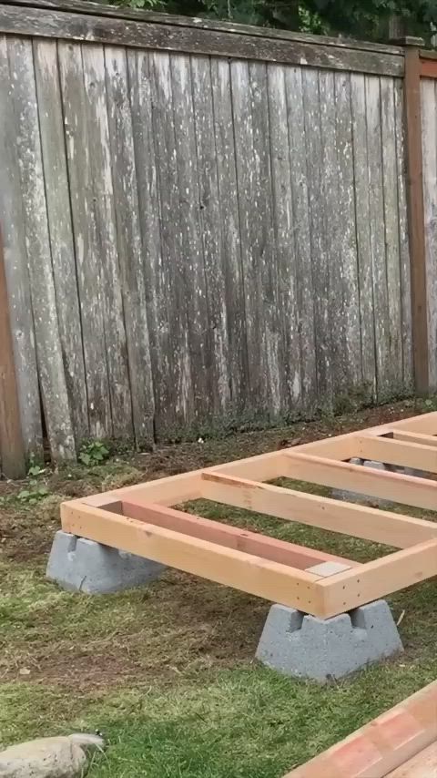 This may contain: a wooden bed frame sitting in the middle of a grass covered yard next to a fence