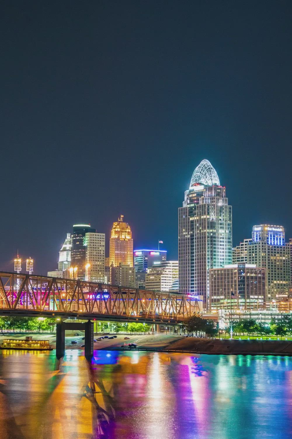 This may contain: the city skyline is lit up at night with lights reflecting on the water and bridge