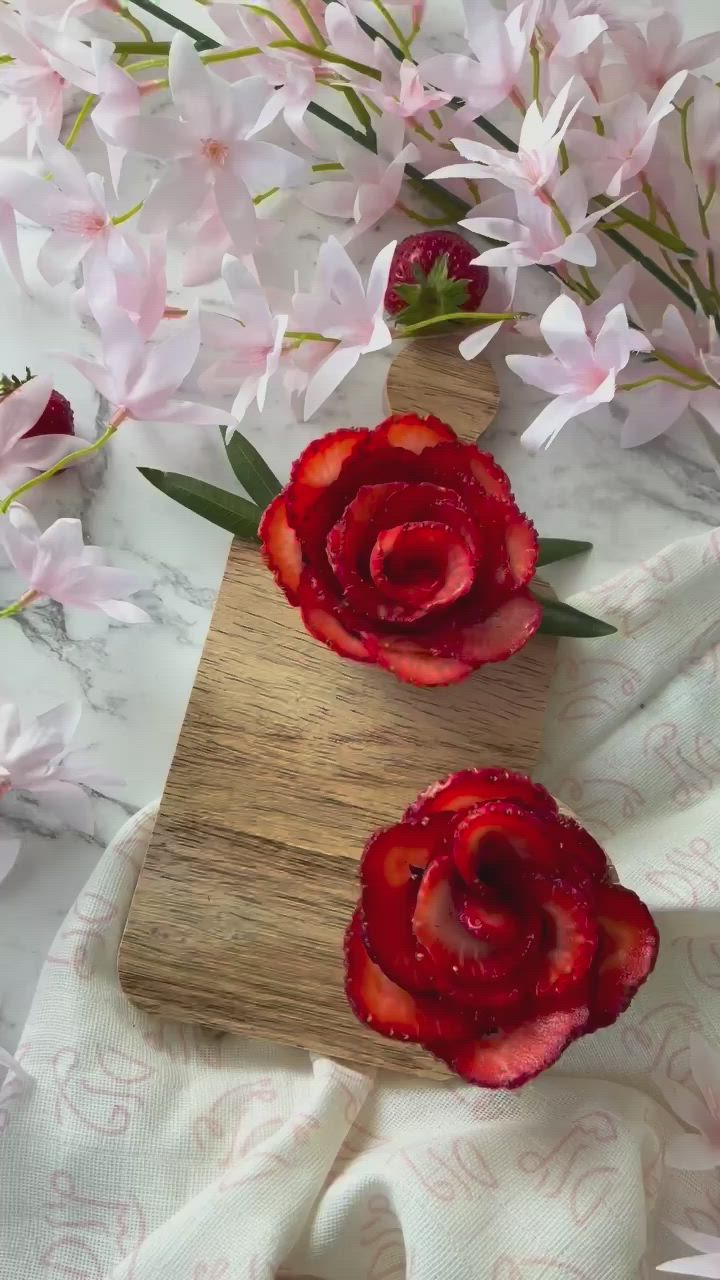 This may contain: two red flowers sitting on top of a wooden cutting board next to pink flowers and white cloth