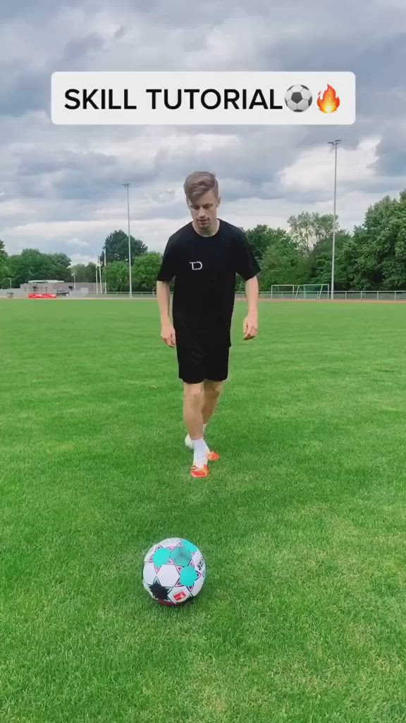 This may contain: a man in black shirt kicking a soccer ball on field with sky and clouds behind him