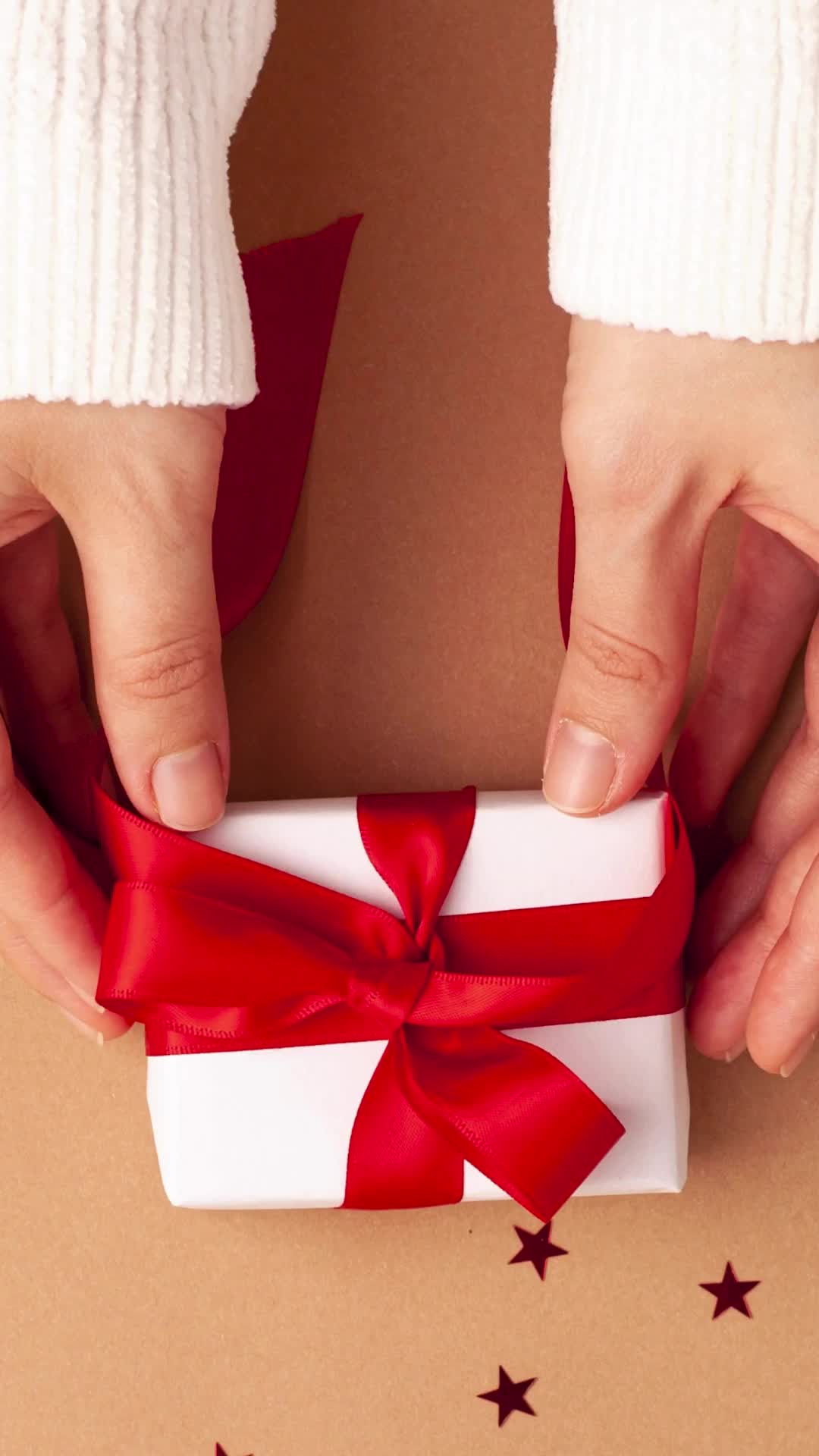 This may contain: a person opening a gift box with a red ribbon on it and stars around the wrapping paper