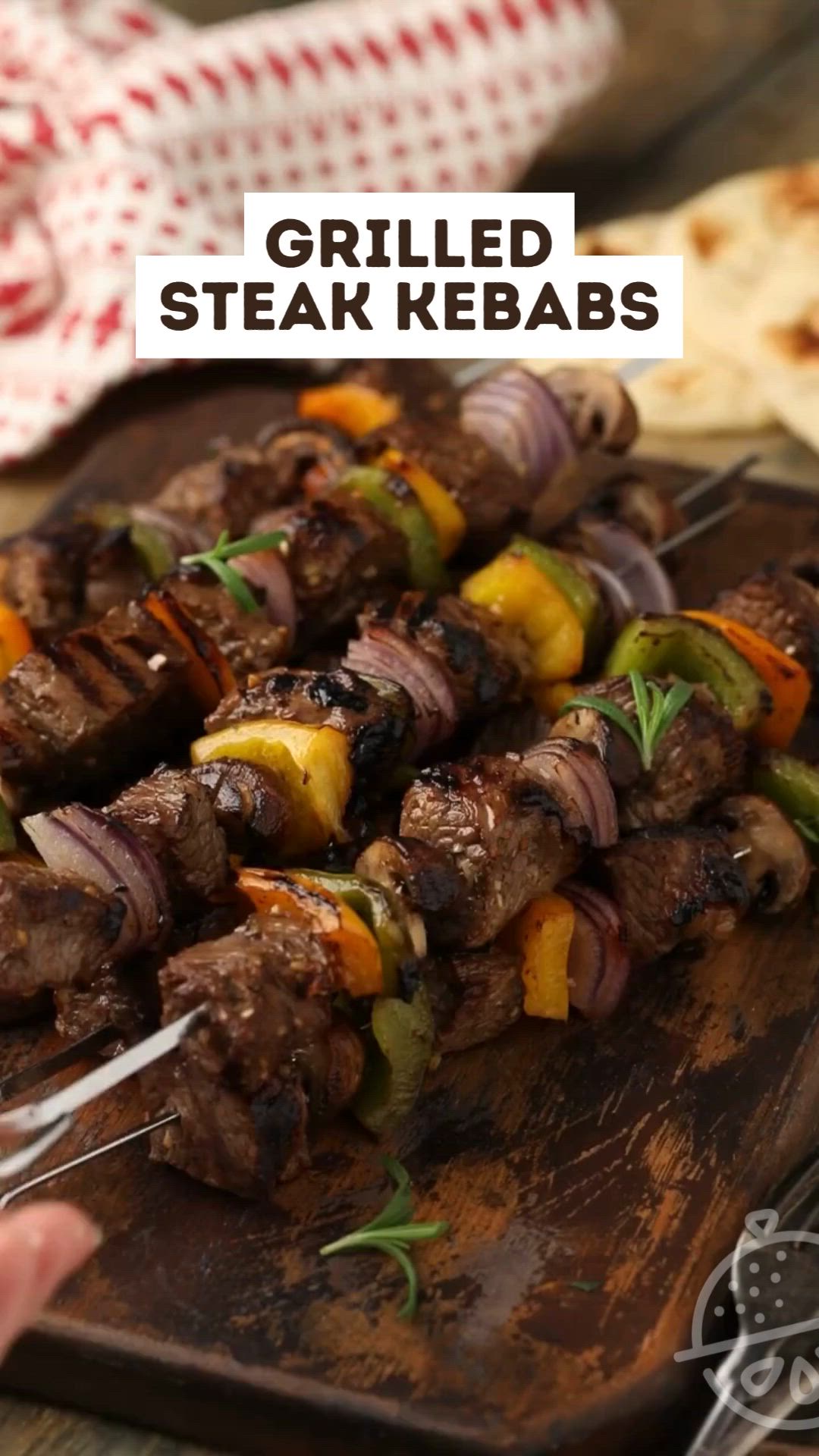 This may contain: a wooden cutting board topped with meat and veggies on skewers next to pita bread