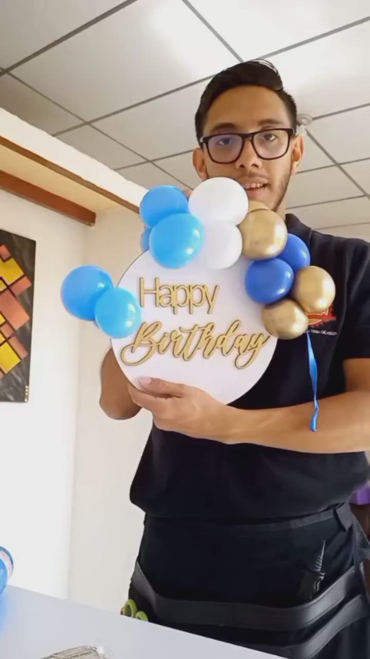 This may contain: a man holding up a happy birthday sign with balloons on it in front of him