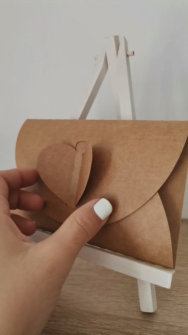 This may contain: a hand holding a piece of brown paper with a heart on it and an envelope in the middle