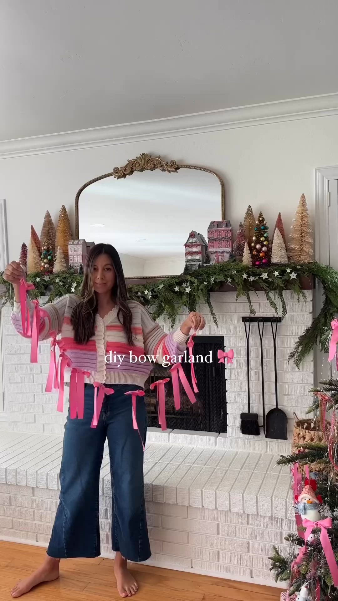 This may contain: a woman standing in front of a fireplace with pink ribbon around her waist and holding a sign that says, my bow stand