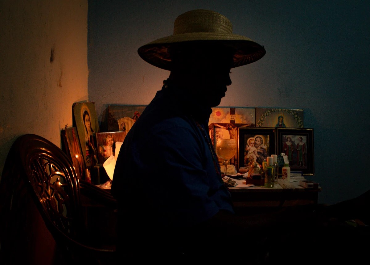 Abel José de 43 anos é um sacerdote da Umbanda. Abel José é um homem negro e está com colar de contas, camisa azul de botões e chapéu de palha, ele aparece em frente de um altar com as imagens de Santa Luzia, Cosme e Damião, São Jorge, Nossa Senhora da Conceição, Preto Velho, Iemanjá e da Cabocla Jurema.