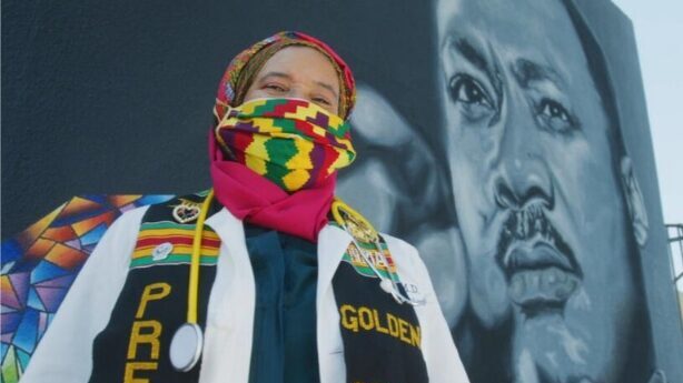 A person in colorful clothing in front of a mural of Martin Luther King Jr.