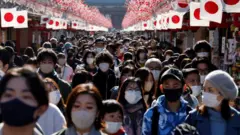 Visitantes con mascarillas protectoras caminan bajo las decoraciones para el Año Nuevo en la calle Nakamise que conduce al templo Senso-ji en el distrito de Asakusa, un lugar turístico popular, en medio de la pandemia de covid-19 en Tokio, Japón