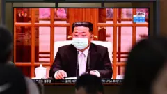 People sit near a screen showing a news broadcast at a train station in Seoul on May 12, 2022, of North Koreas leader Kim Jong Un appearing in a face mask on television for the first time to order nationwide lockdowns after the North confirmed its first-ever Covid-19 cases.