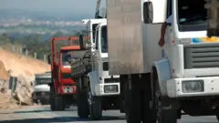 Sequência de quatro caminhões circulando em estrada