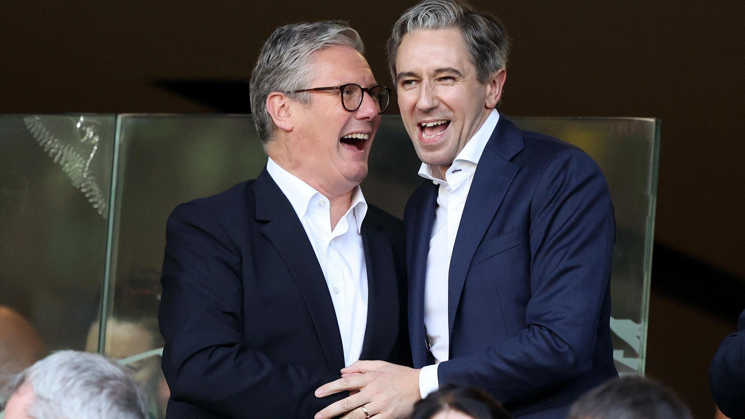 Sir Keir Starmer and Simon Harris clasping hands and laughing in the Aviva stadium stands before the Republic of Ireland v England football match