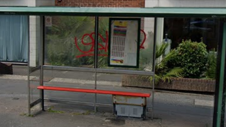 Bus stop with red bench. The clear panel behind the bench has red graffiti sprayed in it