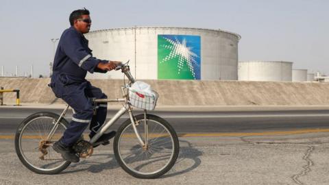 A worker rides a bicycle by oil tanks at an oil processing facility of Saudi Aramco.